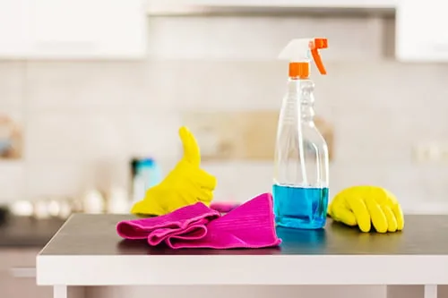 Spray bottle, cloth and cleaning gloves laid out on a kitchen counter