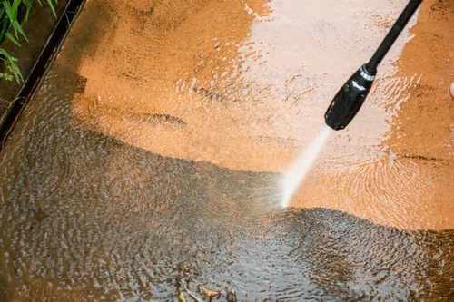 Pressure washer rinsing algae and grime from an exterior concrete surface