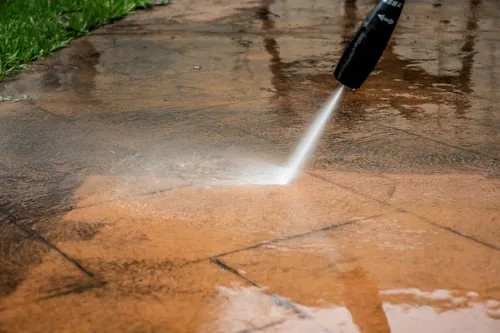 Pressure washer rinsing dirt from a paved driveway to reveal clean stone