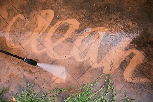 Pressure washer cutting clean lines through grime on a stamped concrete patio